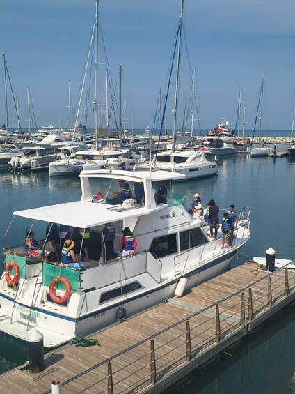 A marina with several boats docked, a wooden pier, and people on a boat. 3