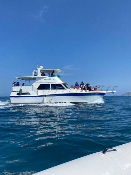 A white and blue boat with people on deck, moving through clear blue water. 1