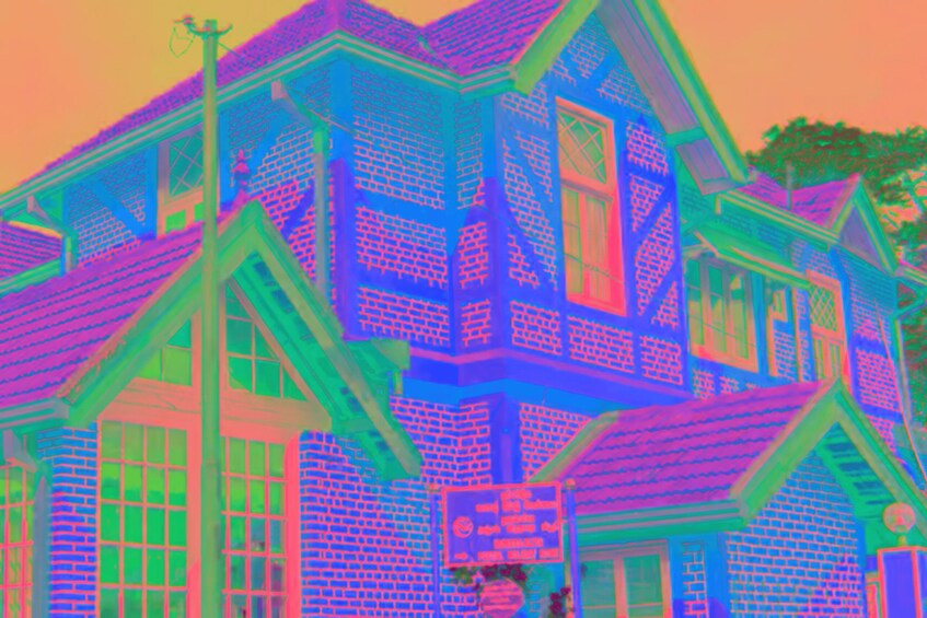 A colorful house with a distinctive blue and green facade, a prominent chimney, and a signboard. 3
