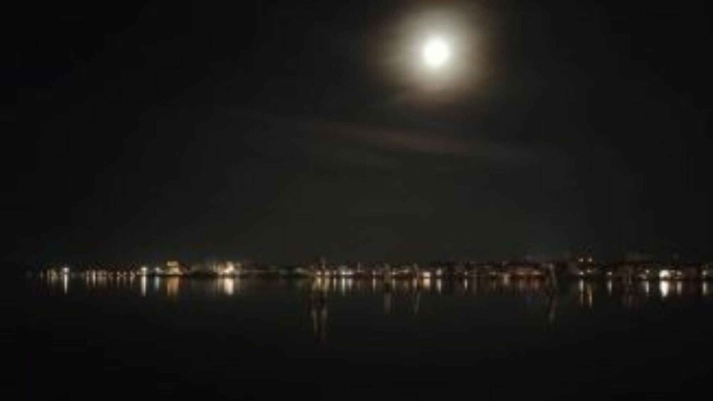 A night scene with a full moon and a calm body of water reflecting city lights. 4