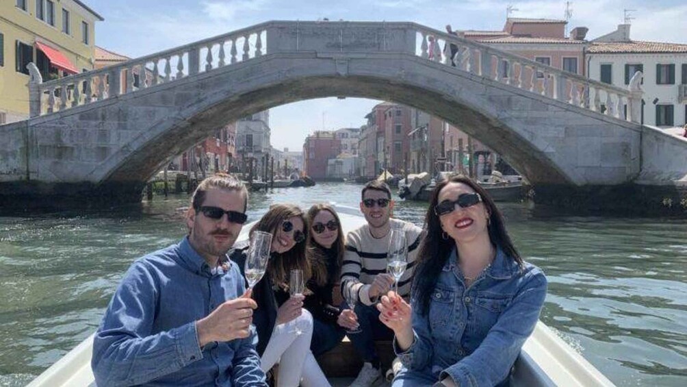A group of people on a boat under a stone bridge in a canal with buildings in the background. 1