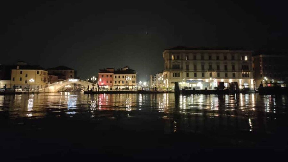 A nighttime view of a canal with buildings and a bridge reflecting on the water. 2
