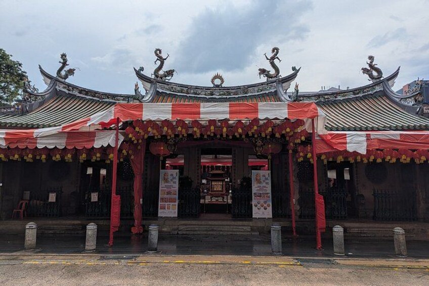 A traditional Chinese building with ornate roof decorations and a red and white entrance canopy. 1