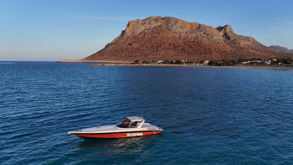 A red and white speedboat on calm blue waters with a rocky mountain in the background. 1