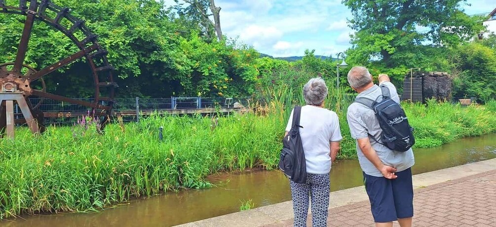 Two people standing by a water feature with a metal structure and greenery. 4