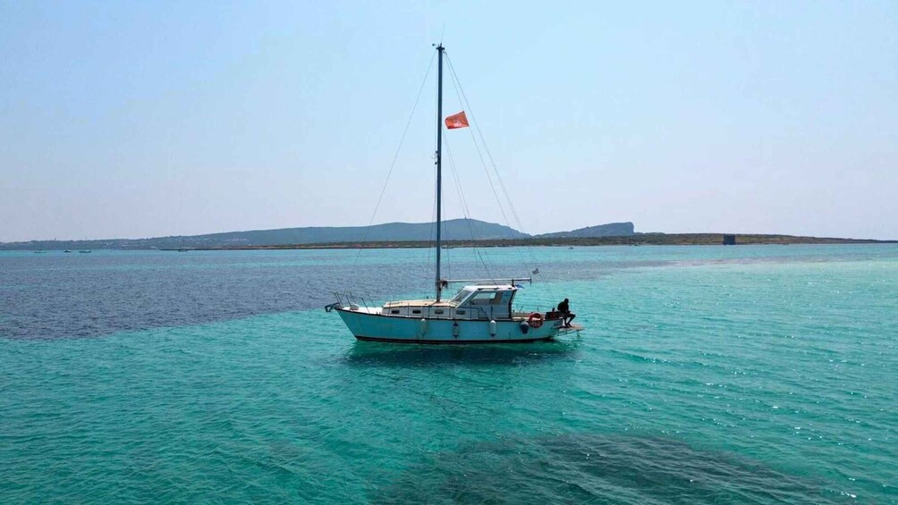 A sailboat with a flag on a calm sea with a distant shoreline. 1