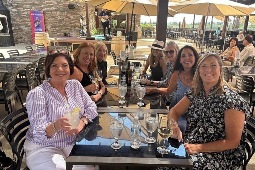 Eine Gruppe von Personen sitzt in einem Restaurant im Freien mit Tischen, Stühlen und Sonnenschirmen. 1