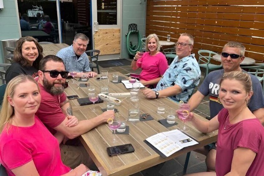 A group of people seated around a wooden table outdoors, with drinks and menus on the table. 4