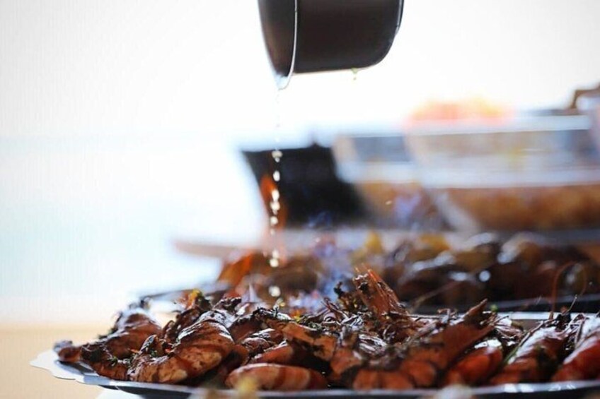 A tray of cooked lobsters being drizzled with sauce. 3