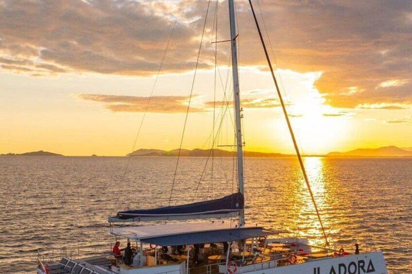 A sailboat named 'Iladora' with a crew, sailing on calm waters during sunset. 2