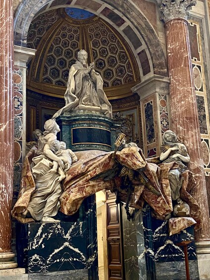 A marble sculpture of a historical figure with a pedestal, set against an ornate ceiling with geometric patterns. 4