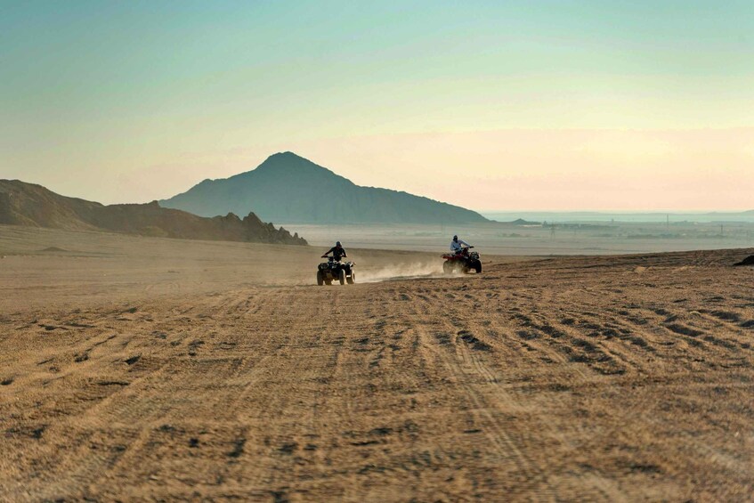 Two off-road vehicles on a dusty terrain with a mountain in the background. 2