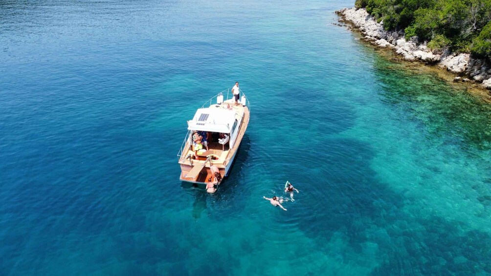 A boat with people on deck and two individuals swimming in clear blue water. 1