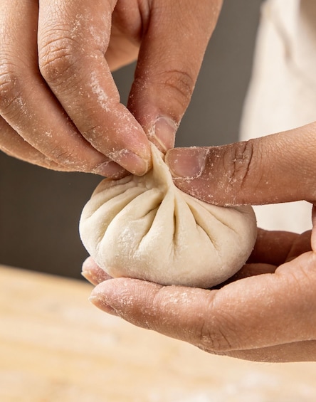 Hands shaping dough into a bun with a pleated design. 4