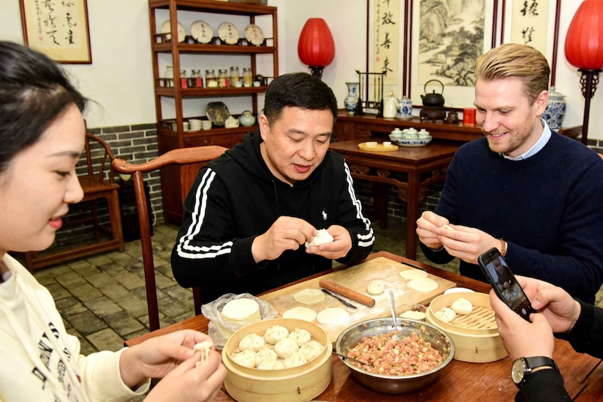 A group of people preparing dumplings at a wooden table with a traditional setting in the background. 5