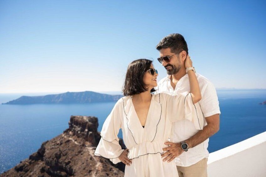 Un couple se tient sur une falaise, surplombant la mer, avec un promontoire rocheux et des îles lointaines en arrière-plan. 2