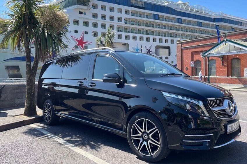 Ein schwarzer Mercedes-Benz Sprinter Van steht auf einer Straße, im Hintergrund ein Kreuzfahrtschiff und ein Gebäude mit einem roten Stern. 4