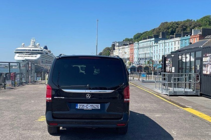 Ein schwarzes Auto steht auf einer Straße, im Hintergrund ein Fährschiff und rechts Gebäude. 5