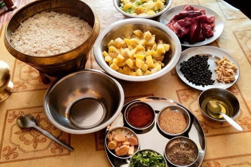 Une table sur laquelle sont disposés divers aliments et épices, notamment un bol de riz, des pommes de terre coupées en dés, de la viande, des haricots et plusieurs récipients contenant des épices. 1