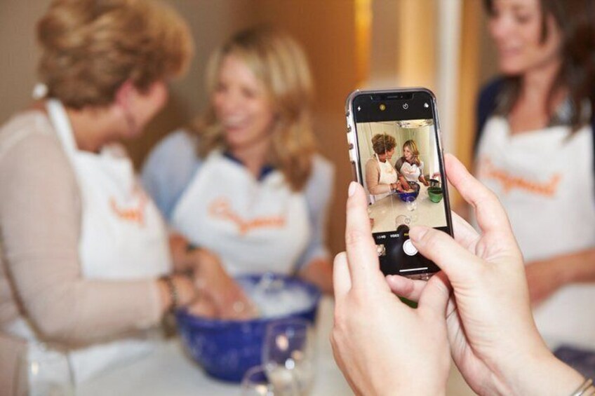 A person holding a smartphone, capturing a group of people in aprons. 2