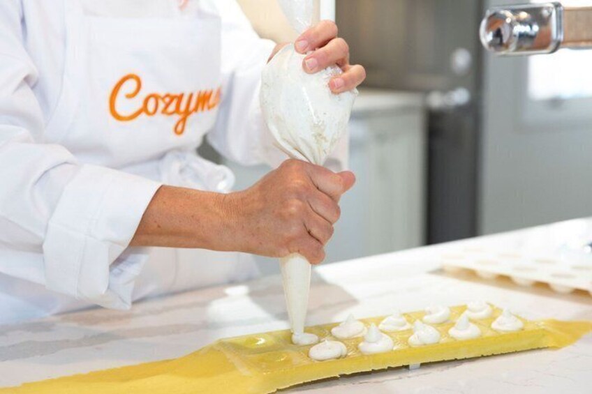A person in a white chef's coat with 'Cozum' on it, piping cream onto a yellow pastry. 3