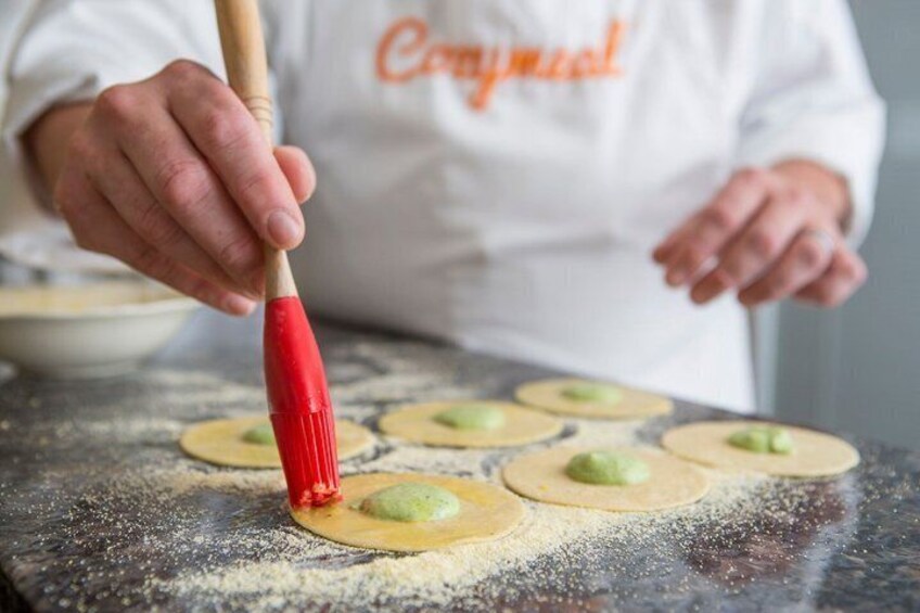 A person in a white chef's coat with orange text, preparing dough with a red-handled rolling pin. 1