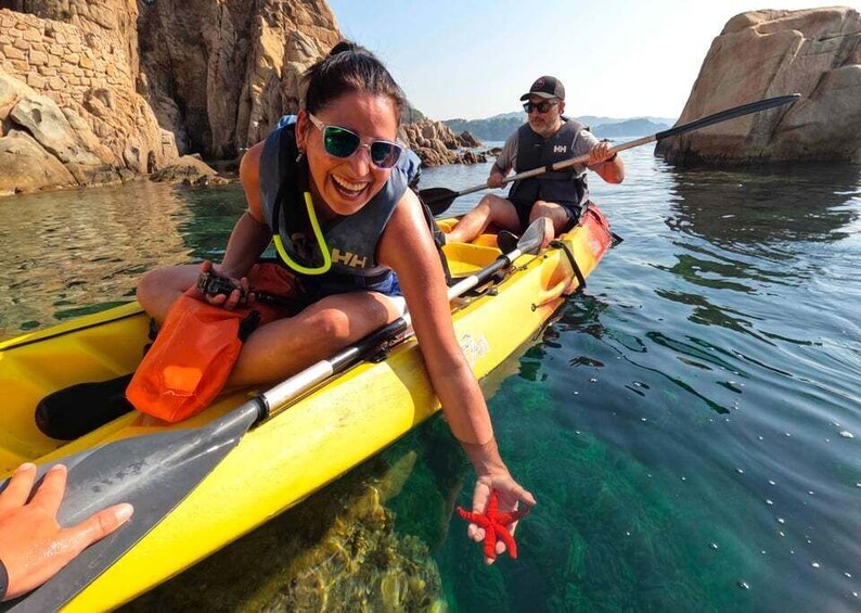 Two people kayaking on clear water with rocky cliffs in the background. 1