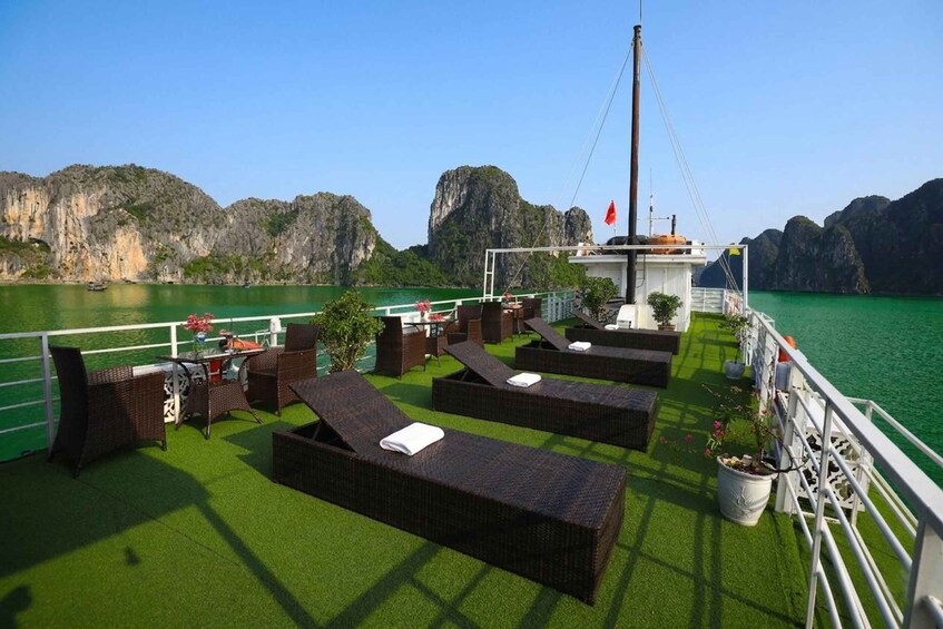A deck with wicker furniture and artificial grass, overlooking a green body of water and rocky cliffs. 3