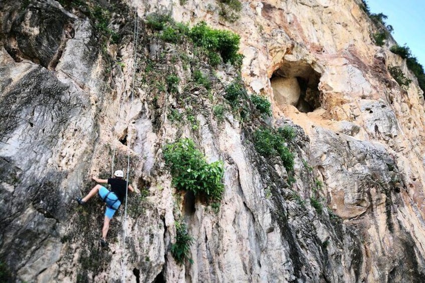 Une personne qui fait de l’escalade sur une paroi rocheuse abrupte, près de l’entrée d’une grotte. 2