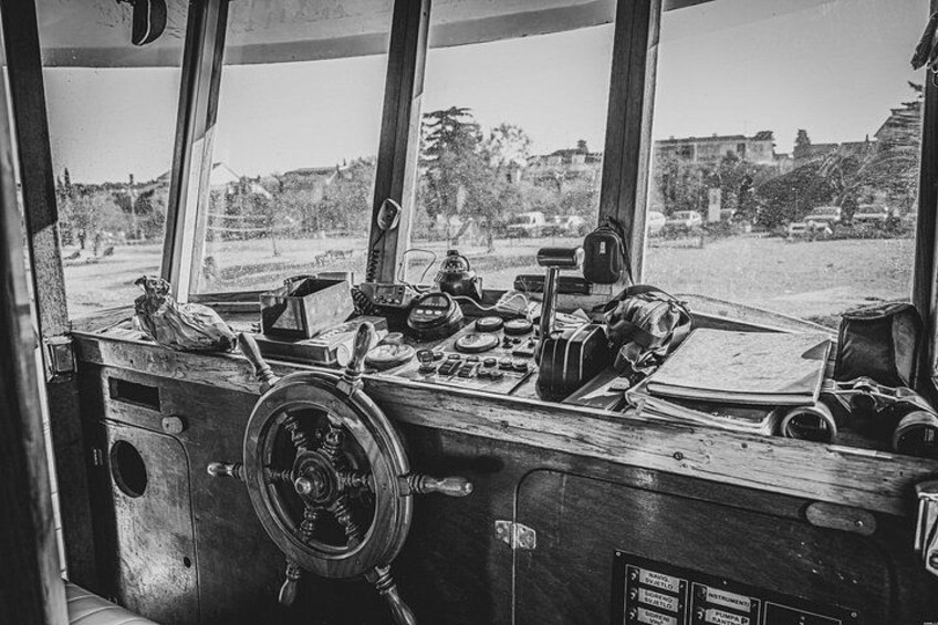 A ship's wheel, various nautical instruments, and a view of the coastline through large windows. 2