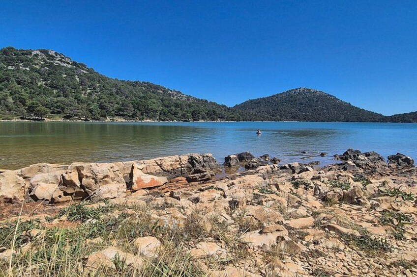 A rocky shoreline with a clear blue lake and hills in the background. 3