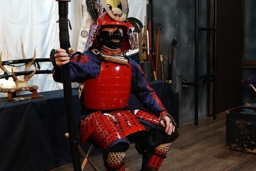 Un individuo vestito con un'armatura da samurai tradizionale, seduto su una sedia e con una spada in mano. 1