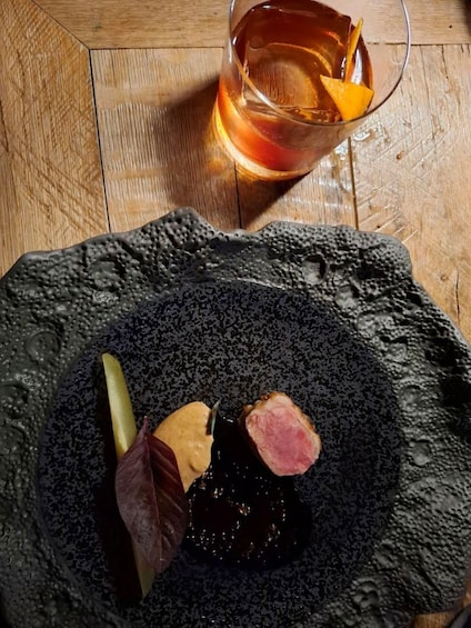 A dark stone plate with a slice of meat, a leaf, and a lemon wedge on a wooden table. 2