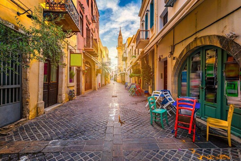 A cobblestone street lined with colorful buildings and chairs. 4
