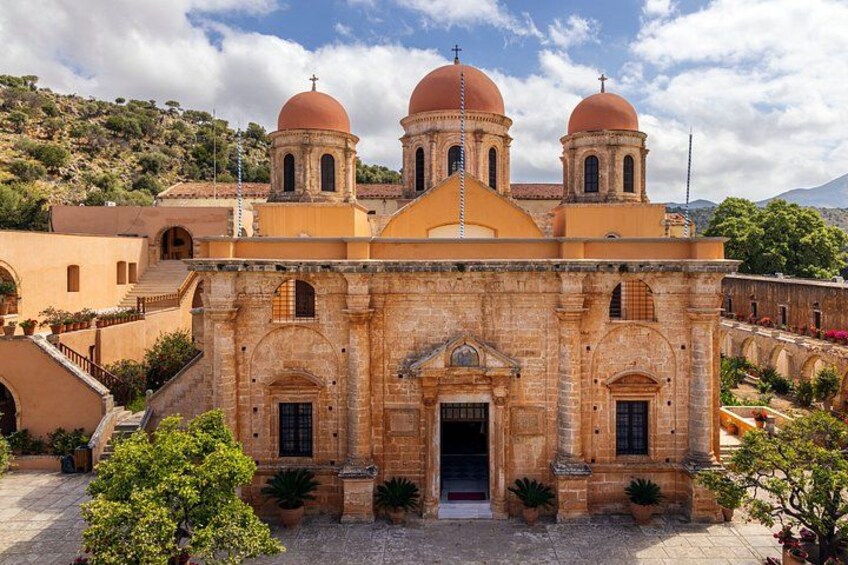 A historic church with three domes, a bell tower, and a courtyard with potted plants. 1