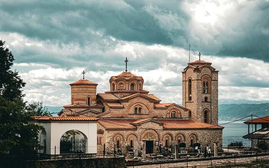 A historic church with multiple domes and a bell tower, surrounded by a stone wall and a body of water. 2