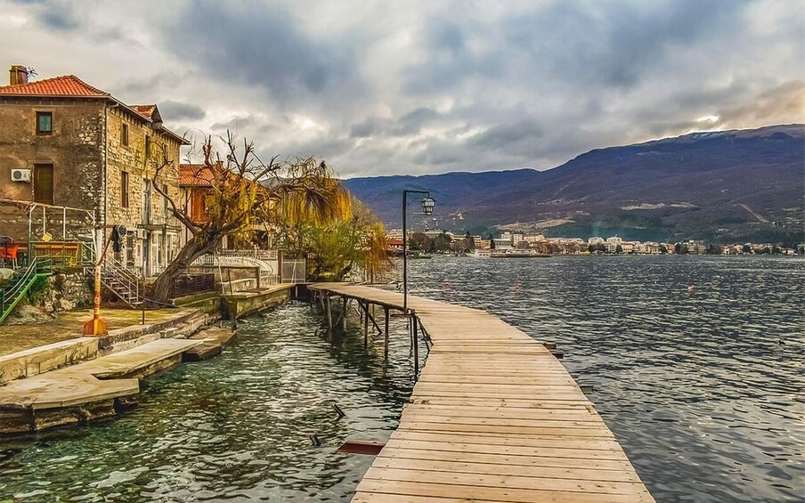 A wooden dock extending into a calm lake, surrounded by stone buildings and a mountain in the background. 3