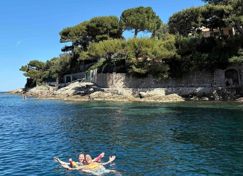 A coastal scene with clear blue water, a rocky cliff with trees, and a stone wall. 4