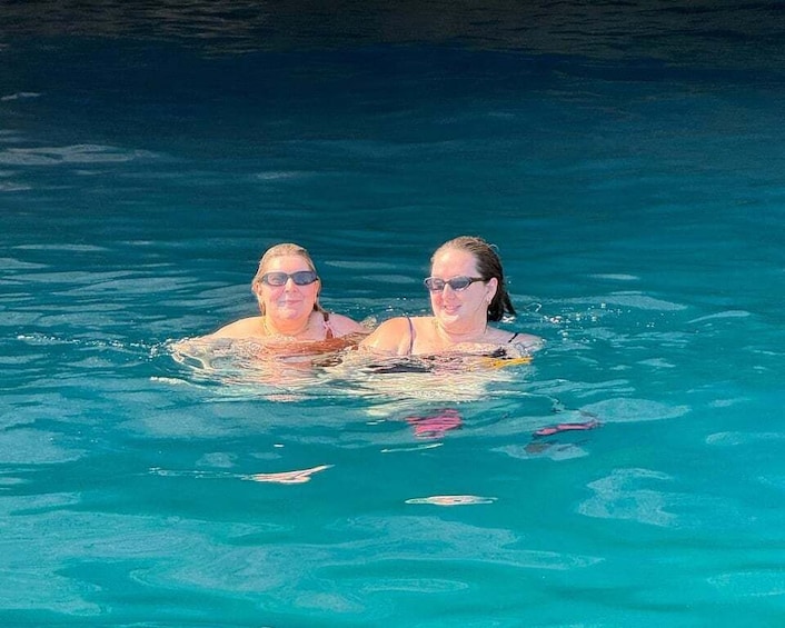 Two people swimming in a clear blue pool. 1