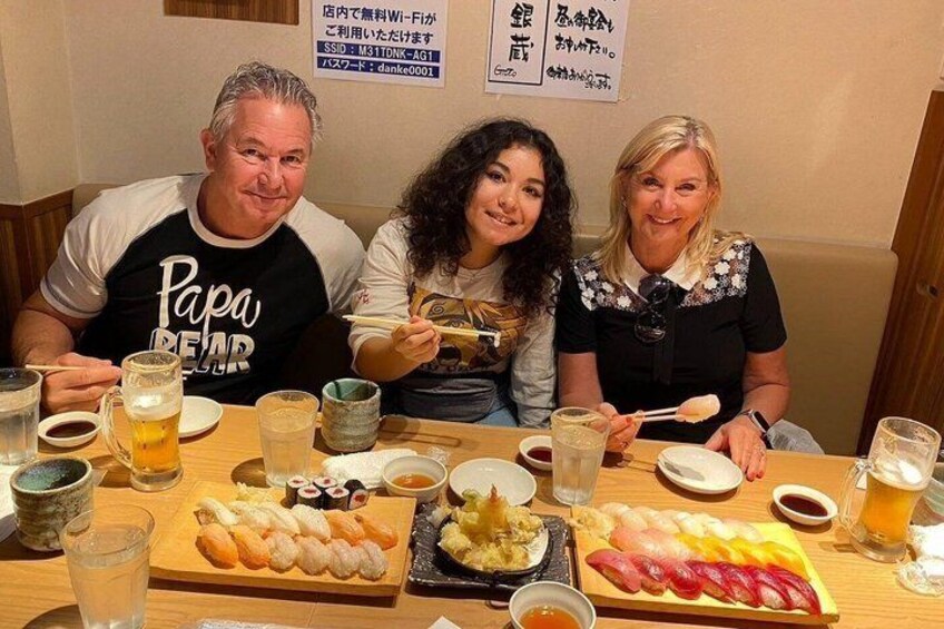Tres personas sentadas en una mesa con comida y bebidas. 3
