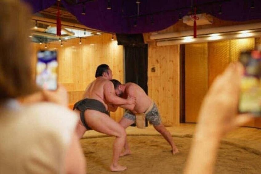 Dos luchadores de sumo en un ring, con espectadores al frente. 1