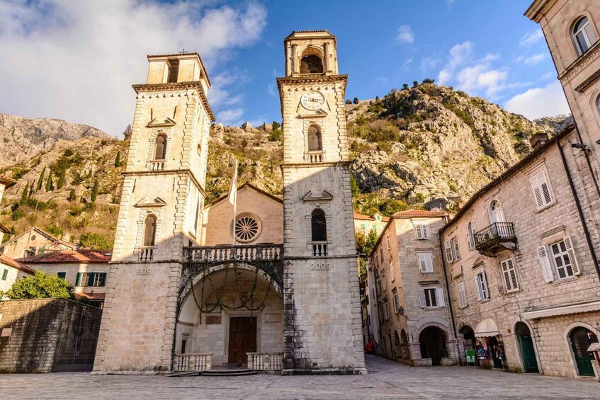 A historic stone church with two towers, an arched entrance, and a mountainous backdrop. 1