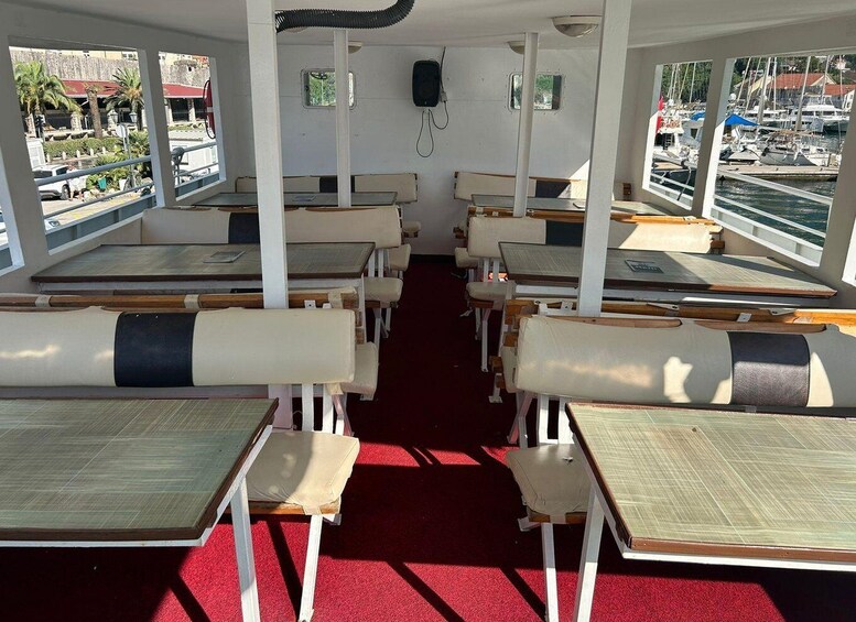 A boat deck with rows of tables and benches, large windows, and a red carpet. 4
