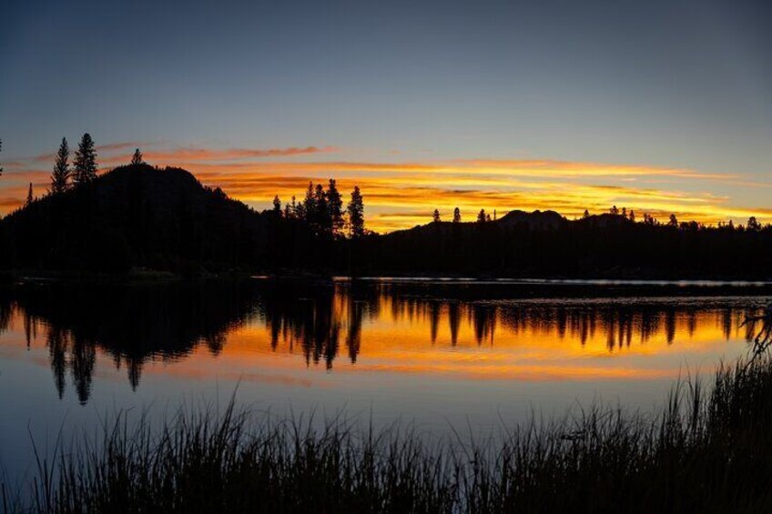 En rolig sø ved solnedgang med silhuetter af træer og en bakke. 4