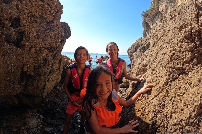 Three individuals wearing life jackets near rocky cliffs by the sea. 3