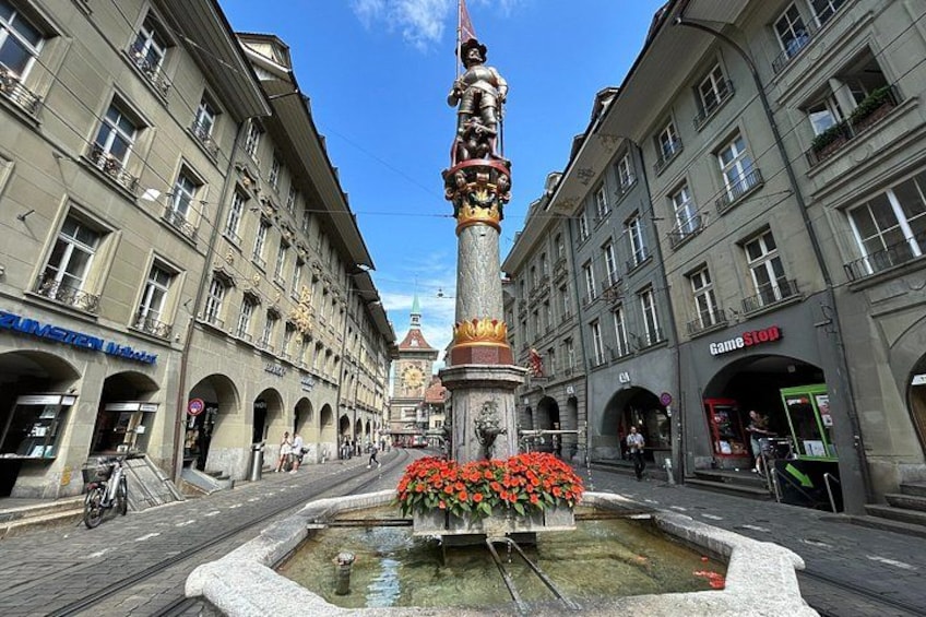 A square with a fountain, buildings, and a clock tower. 4