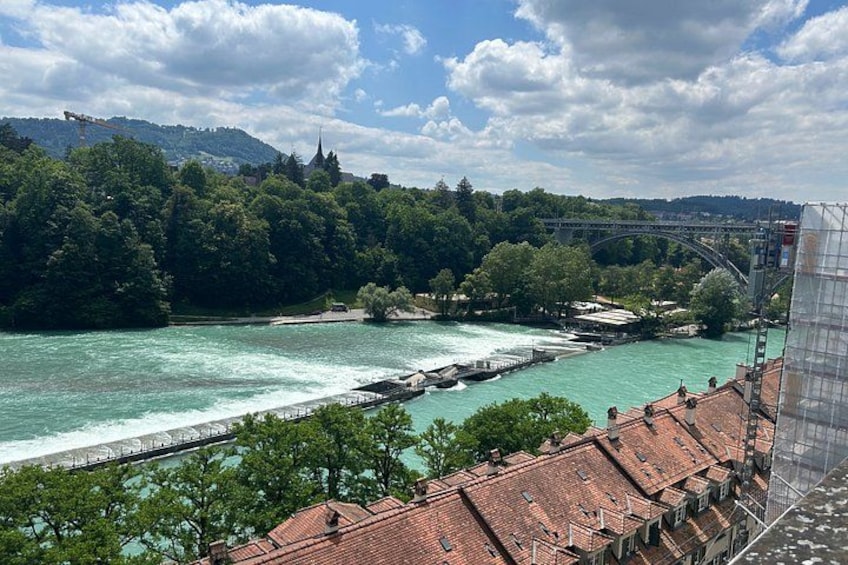 A river with a bridge, a forested hillside, and buildings with red roofs. 2