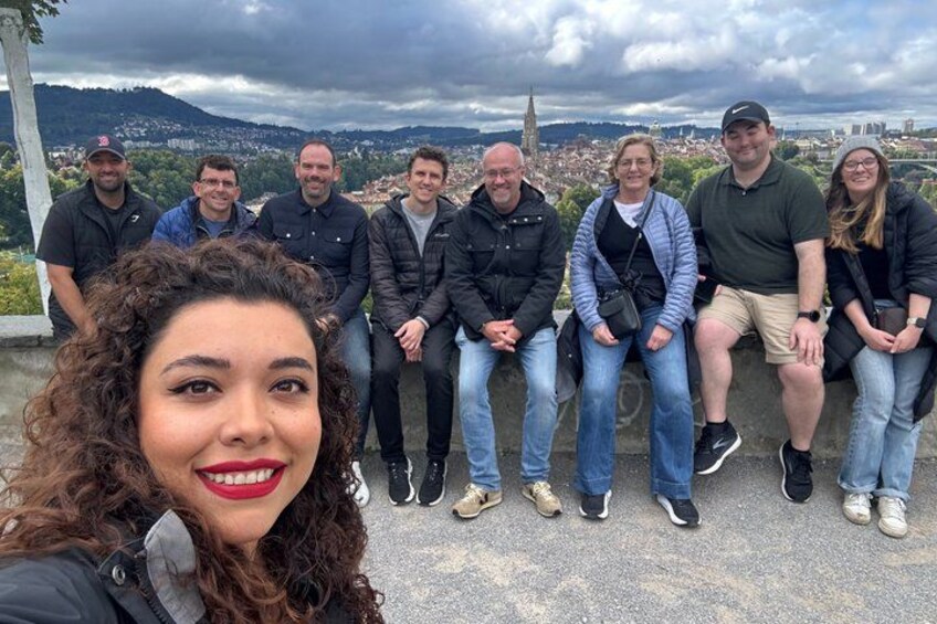 A group of people sitting on a ledge with a cityscape in the background. 1