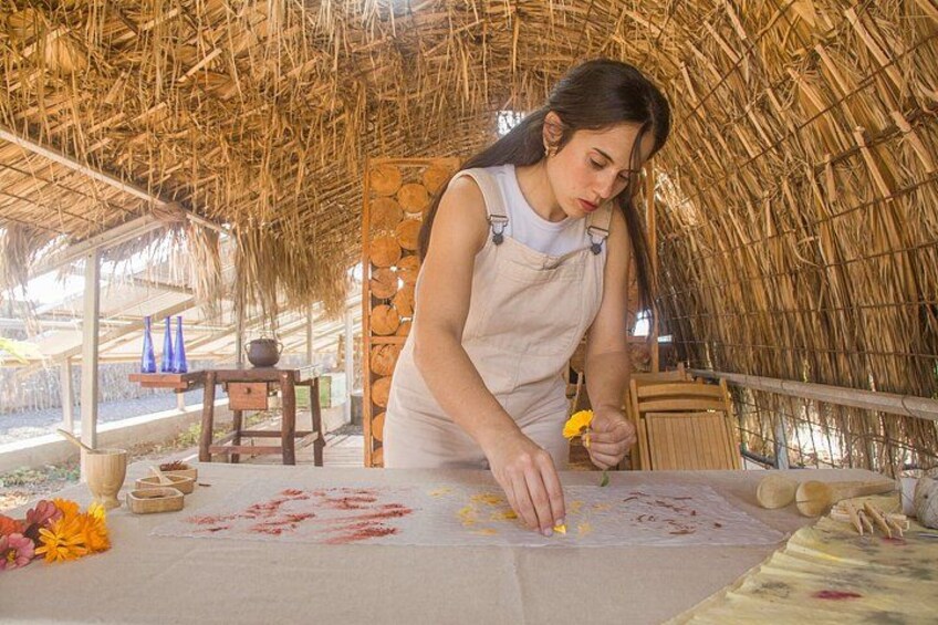 A person painting on a canvas at an outdoor art station with a thatched roof. 1