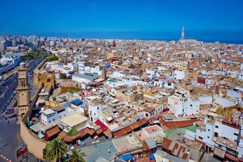 A coastal cityscape with dense urban architecture, a prominent tower, and a clear blue sky. 2